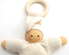 Close up klein wit babypopje in bio katoen, gevuld met bio wol, met houten bijtiring, handgeschilderd gezicht.