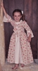 Petite fille souriante portant une robe de princesse blanche avec des bouquets de roses en impression, une sous-jupe blanche, 2 rubans blancs sur les manches longues et 3 rubans fleuris sur la poitrine dans le style de Madame de Pompadour.