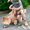 Deux enfants sont assis sur une pelleteuse jouet en bois massief avec laquelle on peut vraiment creuser, accessoire à monter sur le porteur.