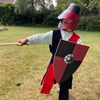 Un enfant joue au chevalier normand avec son épée, bouclier, casque et tabard.